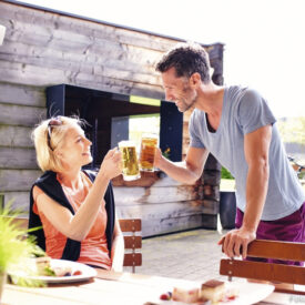 Zwei Gäste stoßen im Freien mit Bier an.