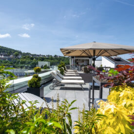 Dachterrasse mit Liegen, Sonnenschirm und Blick auf die Umgebung.