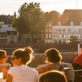 Menschen auf einer Terrasse am Café Maas in Maastricht bei Sonnenuntergang