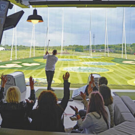 Spieler beim Abschlag vor einer sitzenden Gruppe in einer TOPGOLF-Bay in Oberhausen