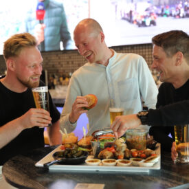 Drei Freunde mit Getränken und Snackplatte beim TOPGOLF in Oberhausen