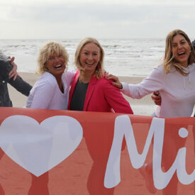 Fröhliche Gruppe hält am Strand von Egmond aan Zee eine Fahne