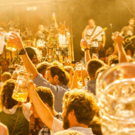 Gäste stoßen mit Maßkrügen vor der Liveband beim Oktoberfest Münster an